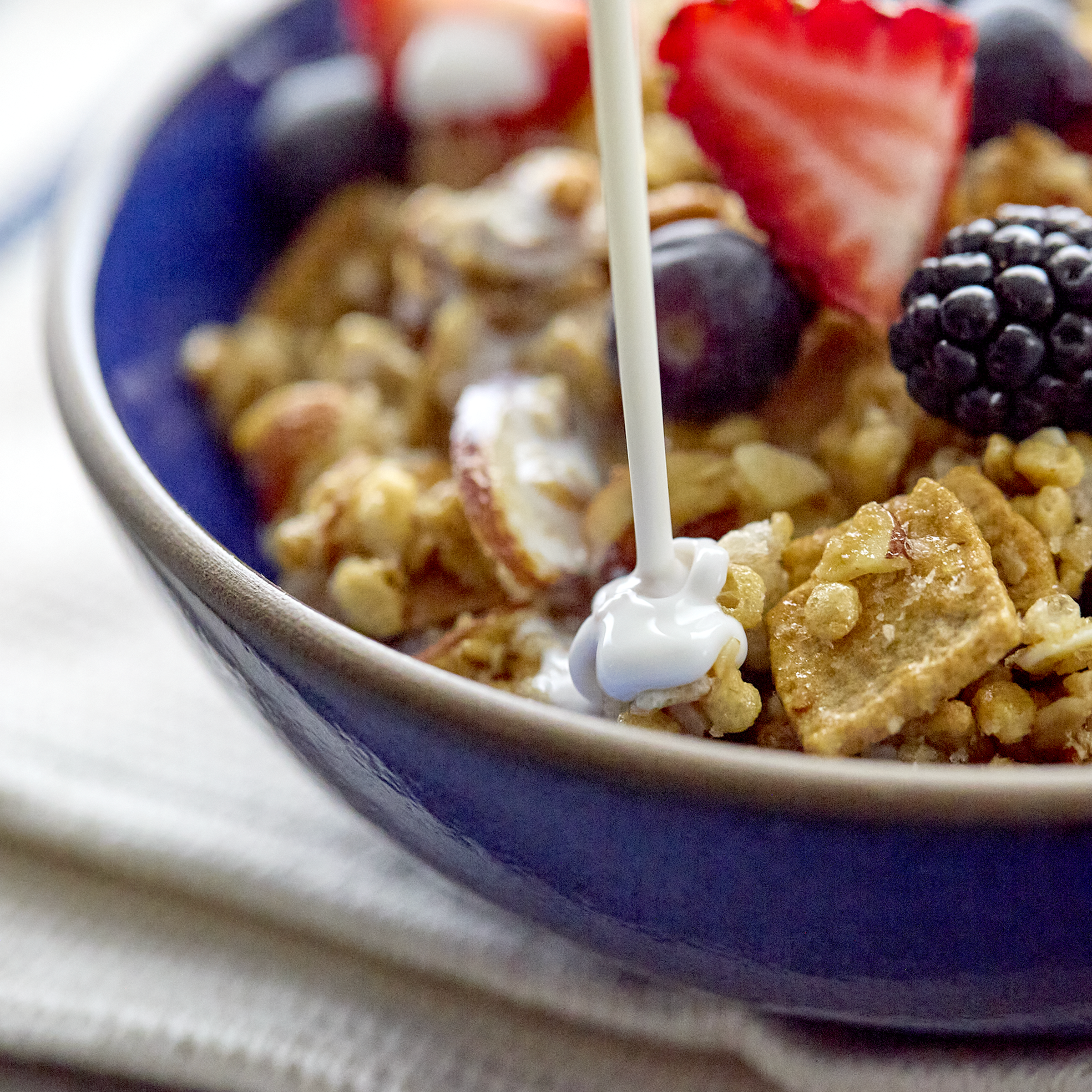 Cereal with milk being poured and berries on a blue plate