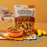 Catalina Crunch Protein Cereal being poured into a bowl with milk, surrounded by bananas on an orange background.