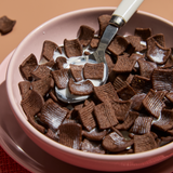 Pink bowl filled with chocolate cereal and a spoon, on a brown background