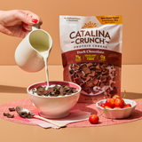 Catalina Crunch protein cereal being poured into a bowl with a pitcher of milk on a peach background.