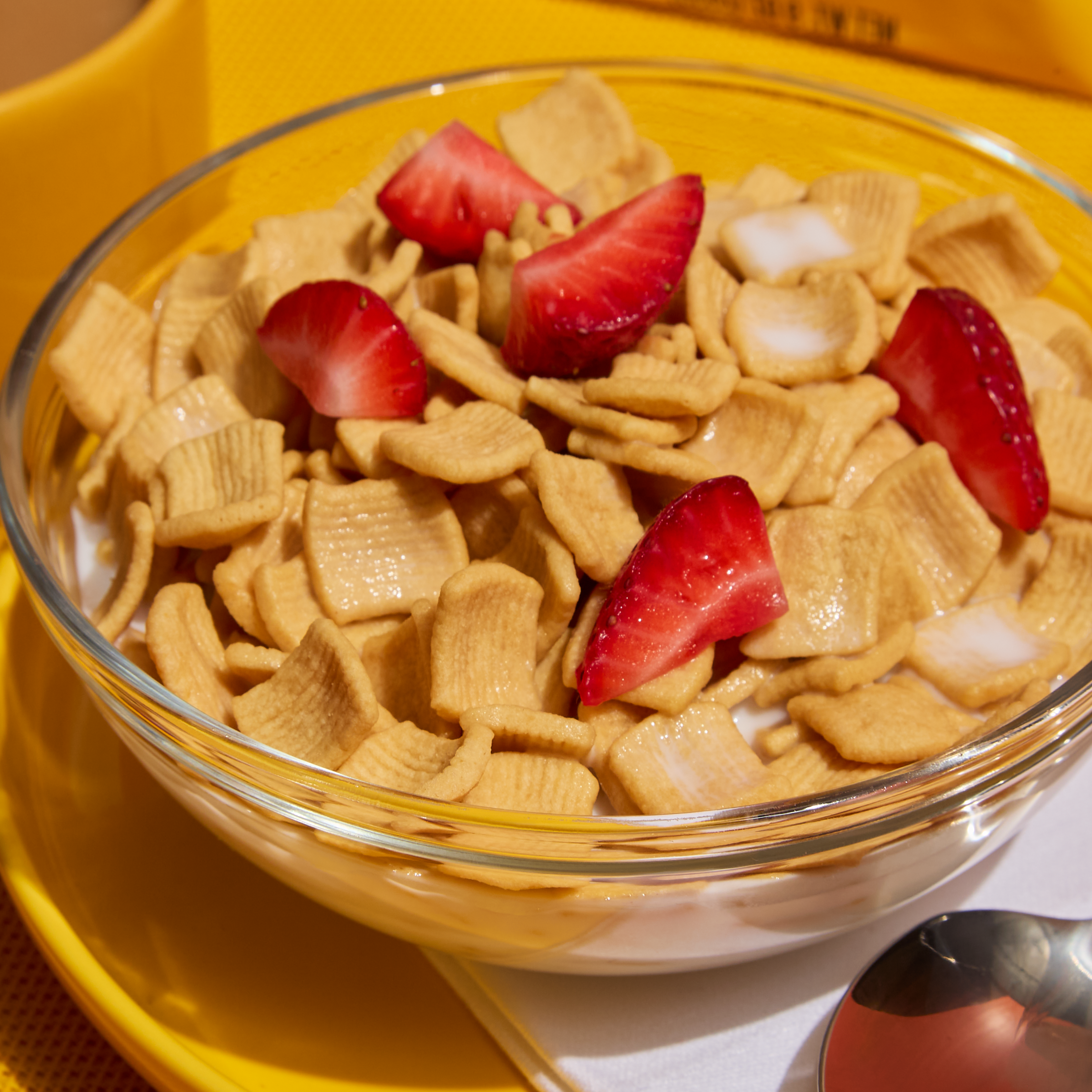 Glass bowl of cereal with strawberries on a yellow plate
