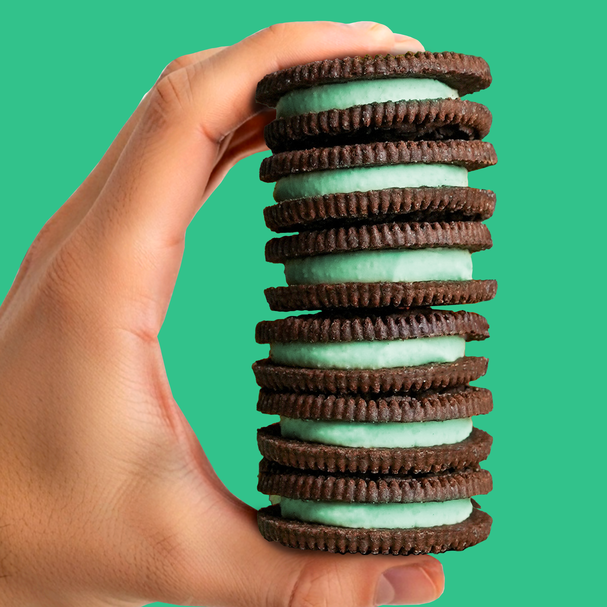 Stack of Oreo cookies held in a hand against a green background