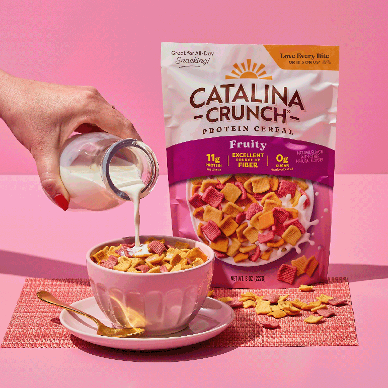 Catalina Crunch Protein Cereal being poured into a bowl with a pink background