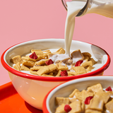 Bowl of cereal with milk being poured, pink background