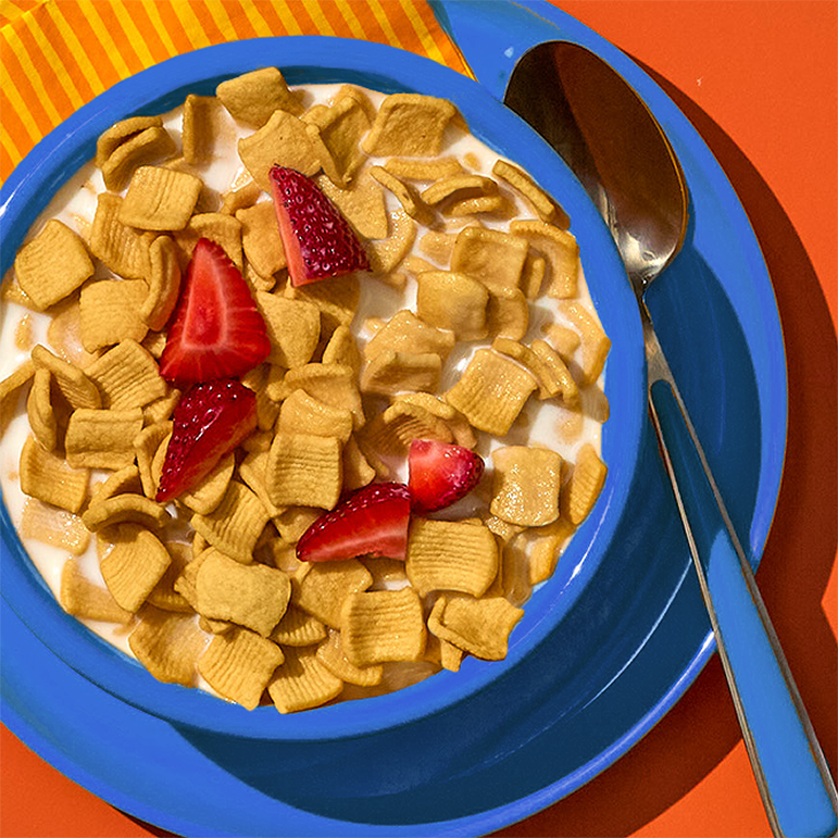 Bowl of cereal with strawberries on a blue plate against an orange background