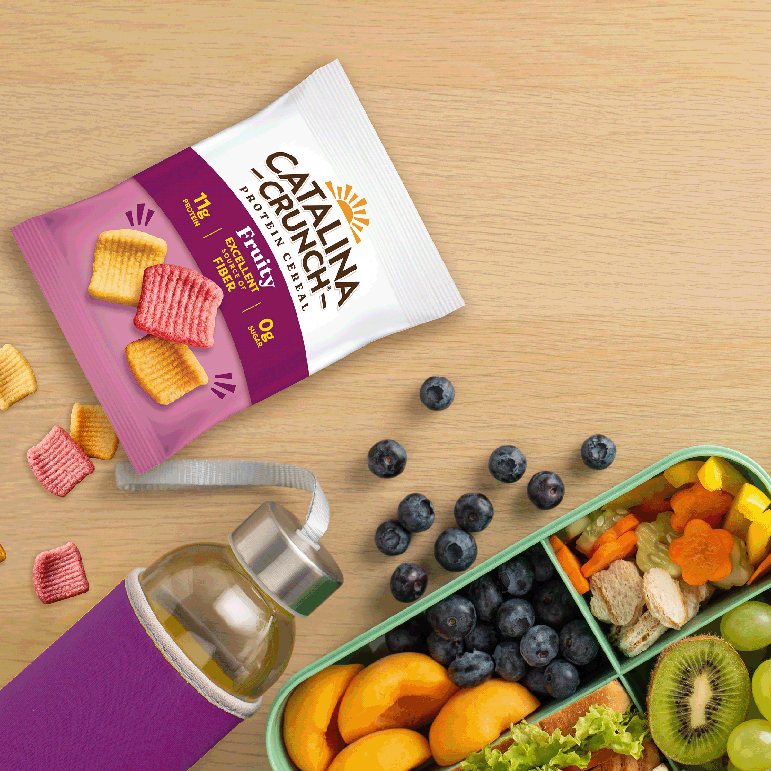 Catalina Crunch snack package on a wooden surface with fruits and a snack container.