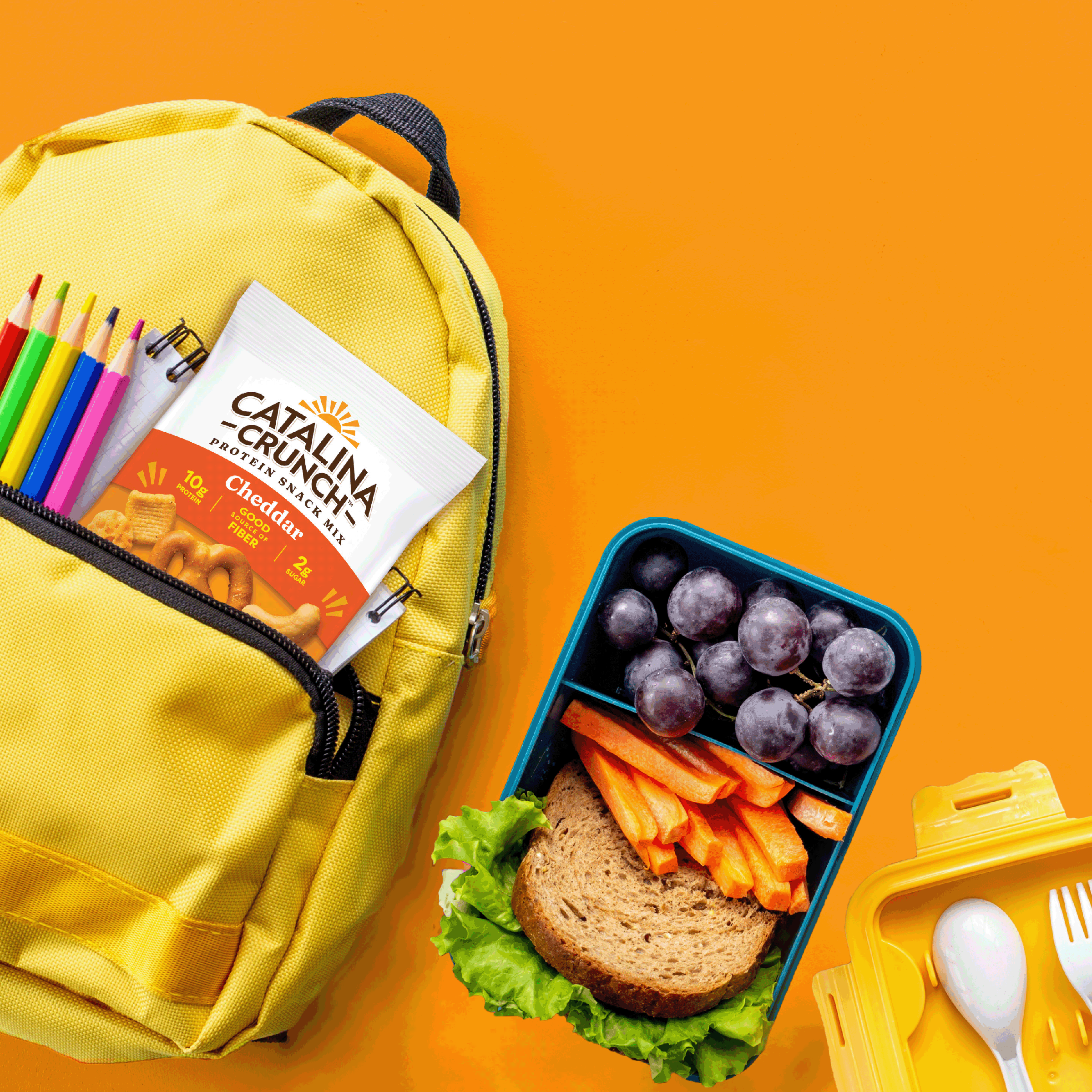 Yellow backpack with school supplies and a lunchbox with a sandwich, carrots, and grapes on an orange background.