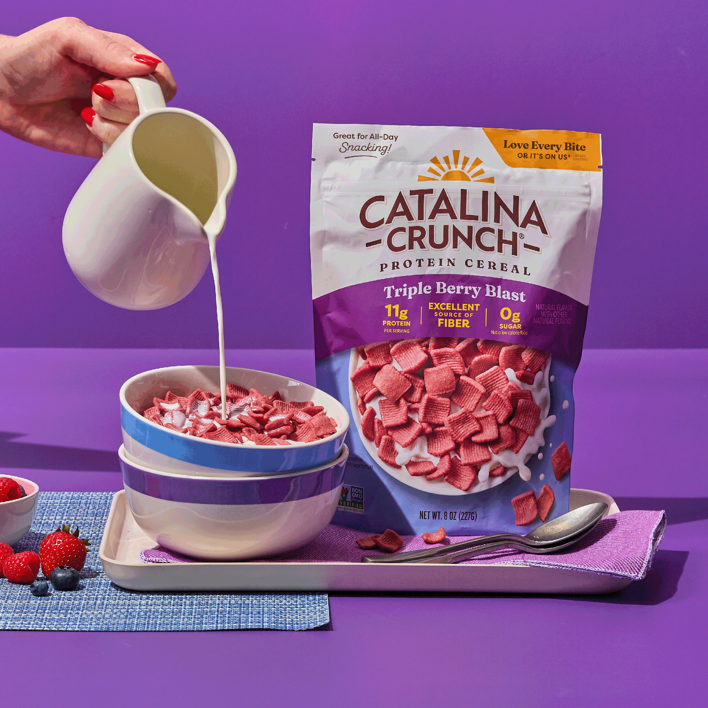 Catalina Crunch Protein Cereal and milk being poured into a bowl with a purple background