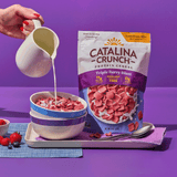 Catalina Crunch Protein Cereal and milk being poured into a bowl with a purple background