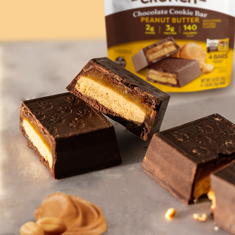 Catalina Crunch chocolate cookie bar with peanut butter filling on a gray surface, with a package of the product in the background.