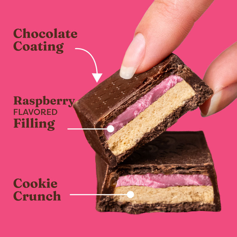 Chocolate-coated dessert with raspberry filling and cookie crunch, held by a hand against a pink background.